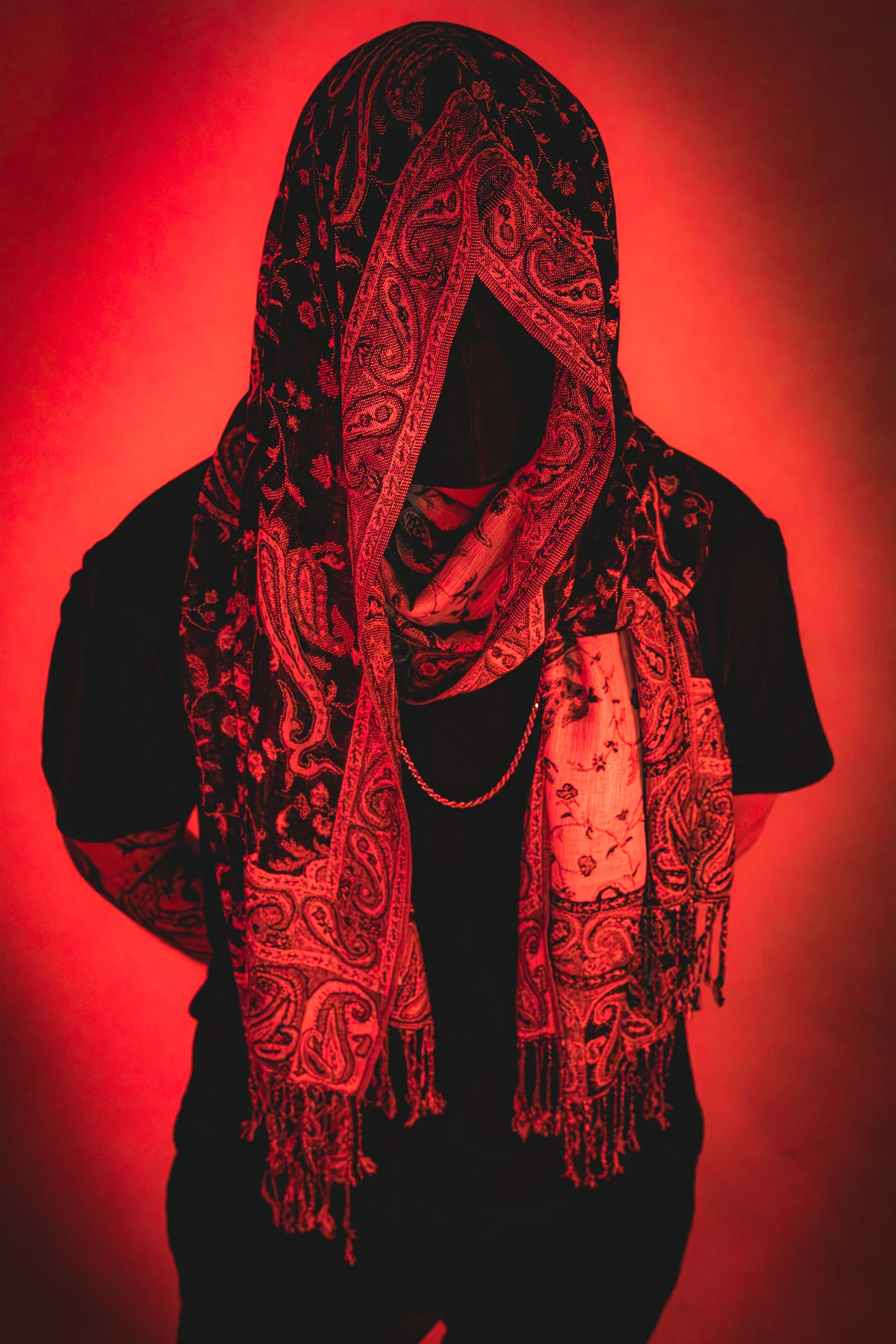 Desert Hydra, masked and hooded, against a red backdrop